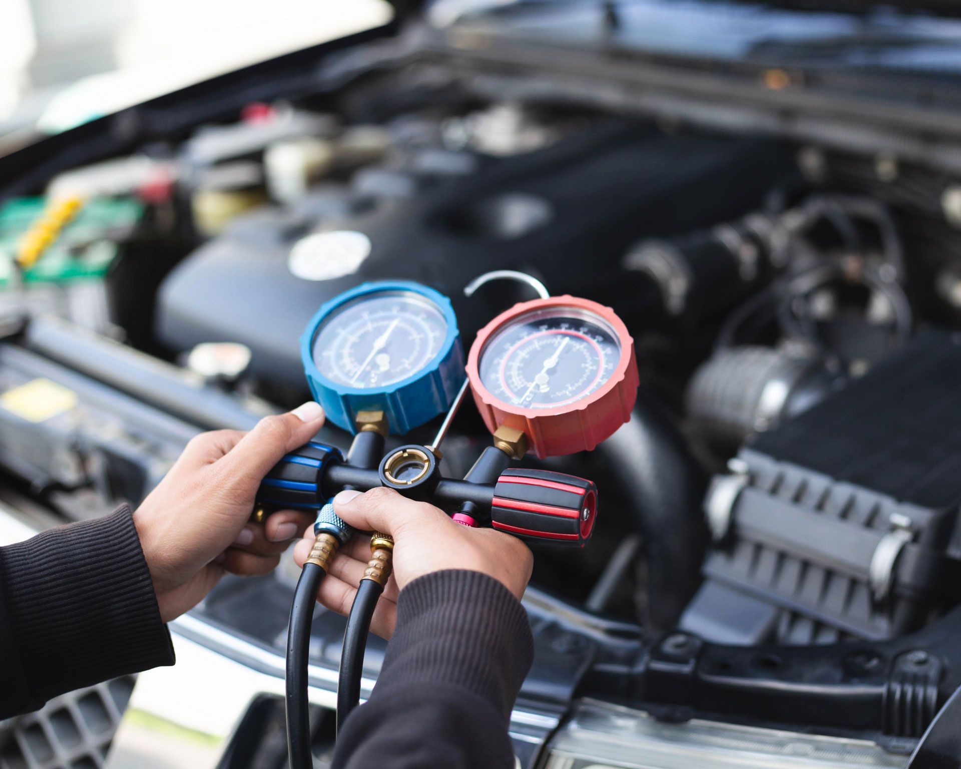 Hands attaching gauges to a car engine. Blue and red gauges, hoses, and engine bay are visible.