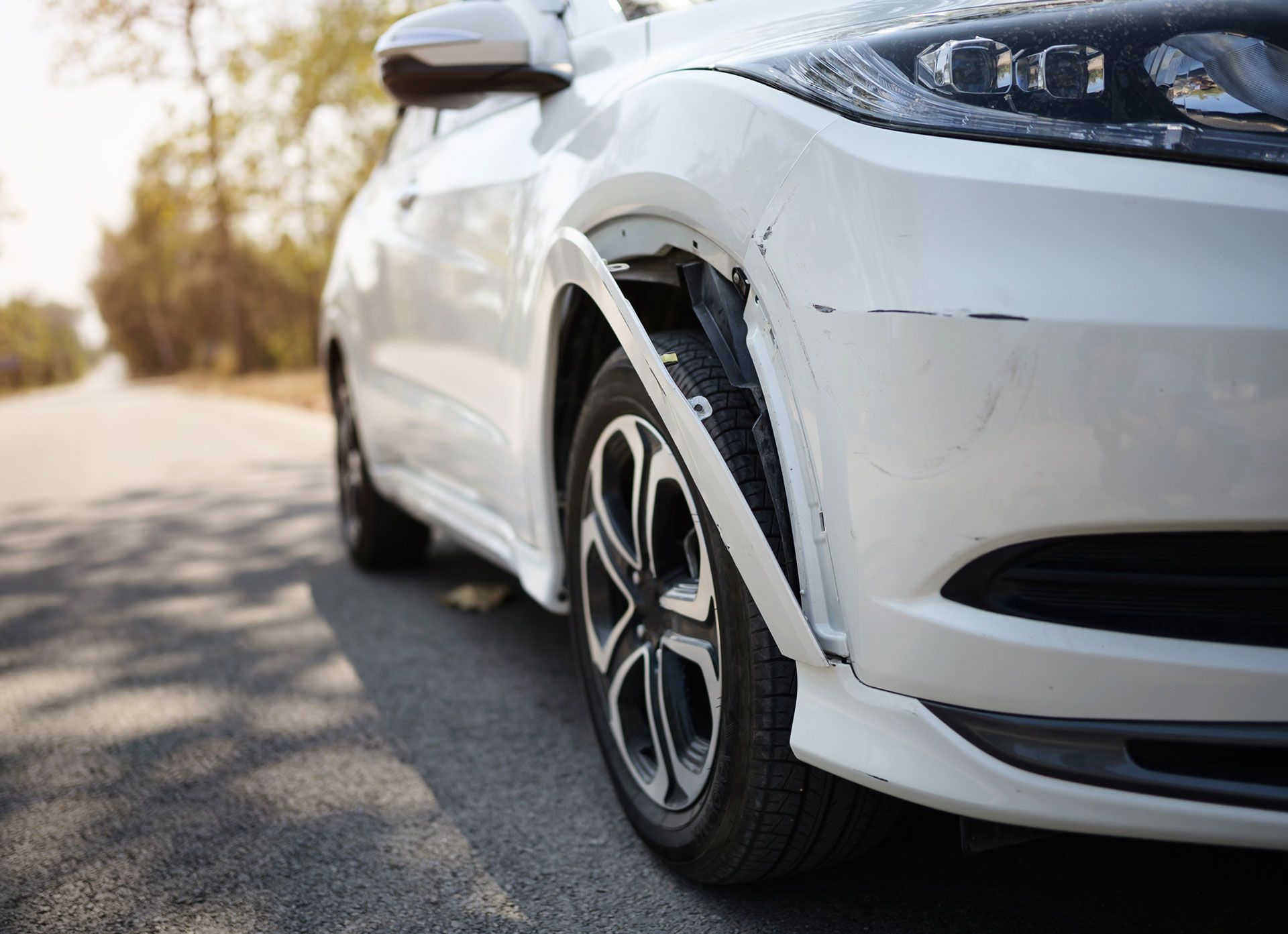White car with damaged front fender, parked on a road.
