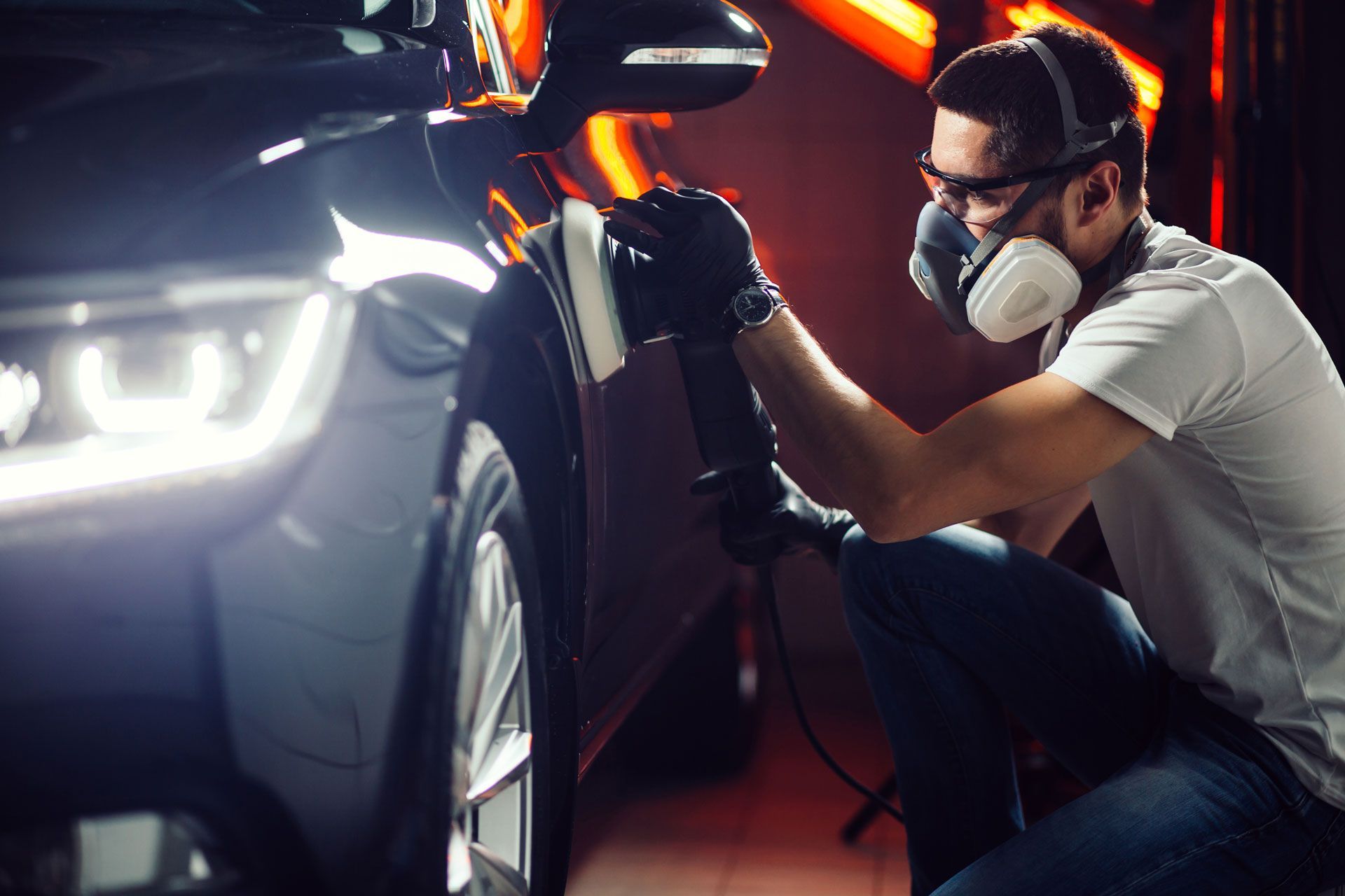 Man polishing a car, wearing a respirator, gloves, and safety glasses.
