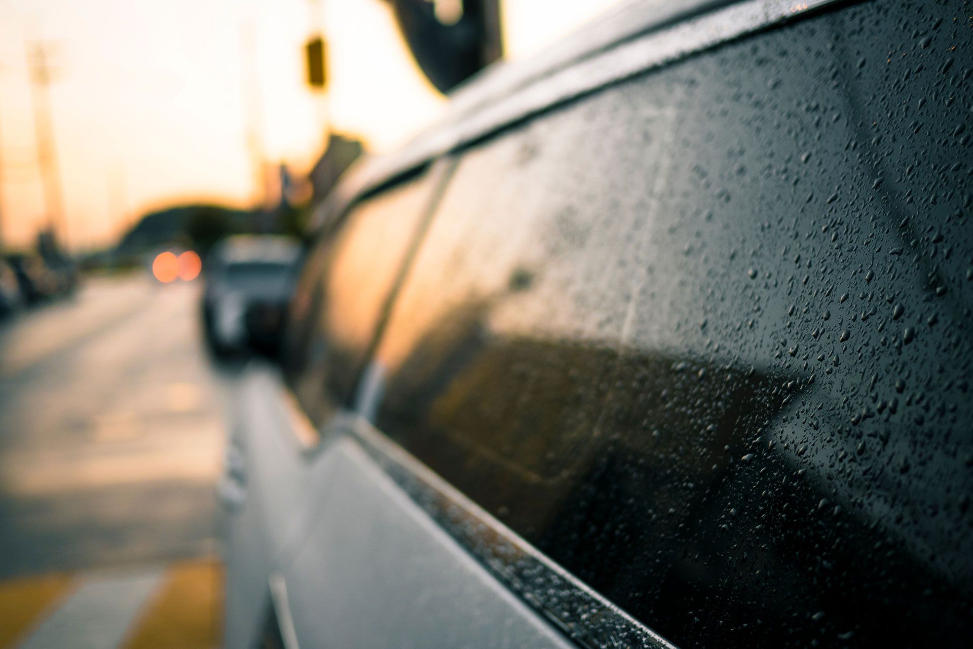 Car window with raindrops, blurred street and sunset in the background.