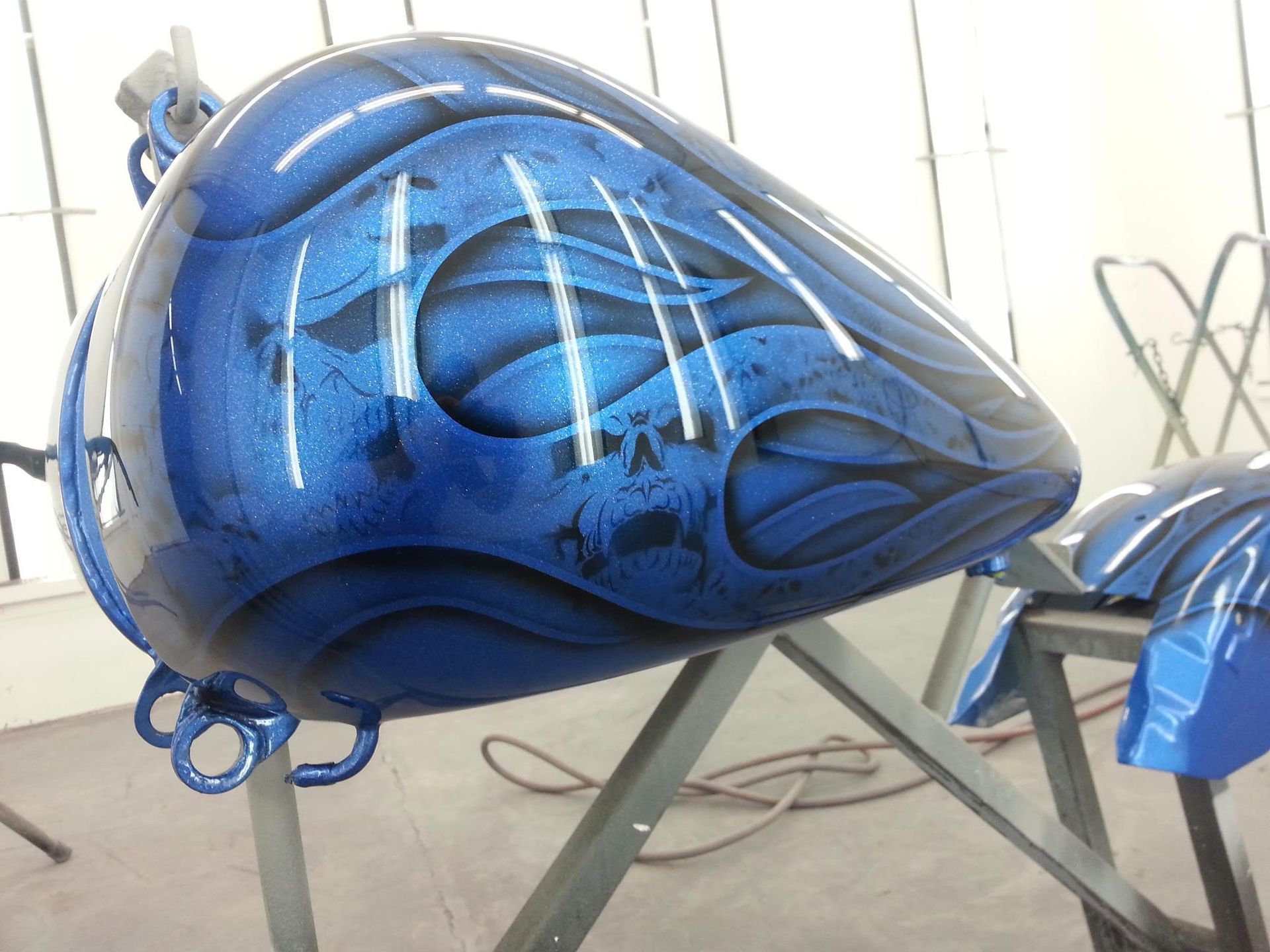 Blue motorcycle gas tank with flames painted on it, resting on a stand.