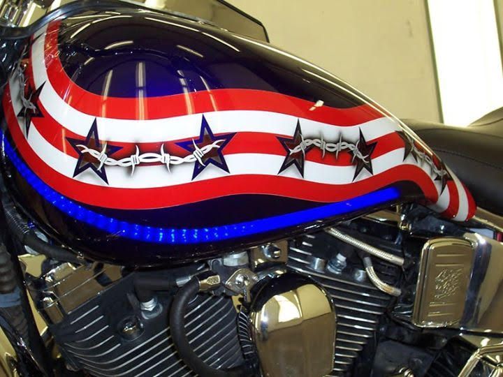 Motorcycle gas tank with a patriotic design: red and white stripes, blue background with star shapes, and barbed wire.