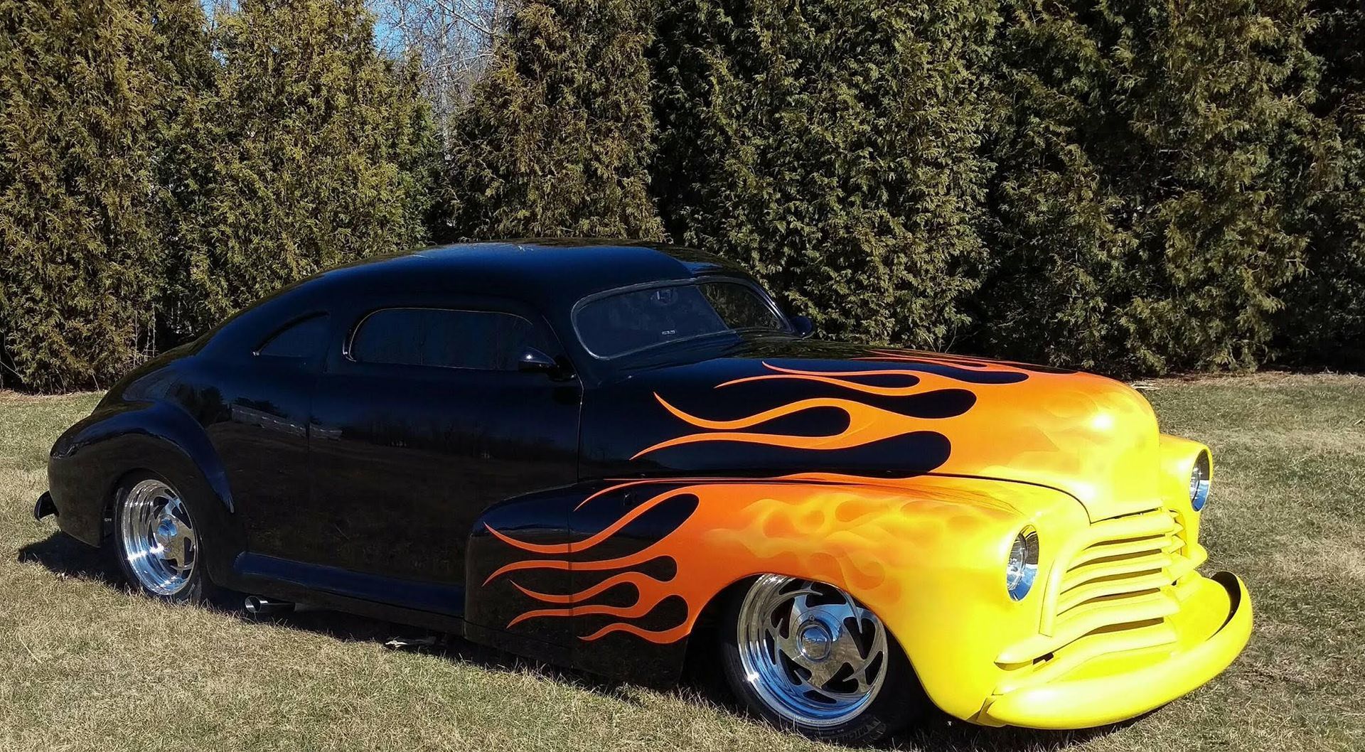 Black and yellow hot rod car with flames painted on the hood and side, parked on grass.