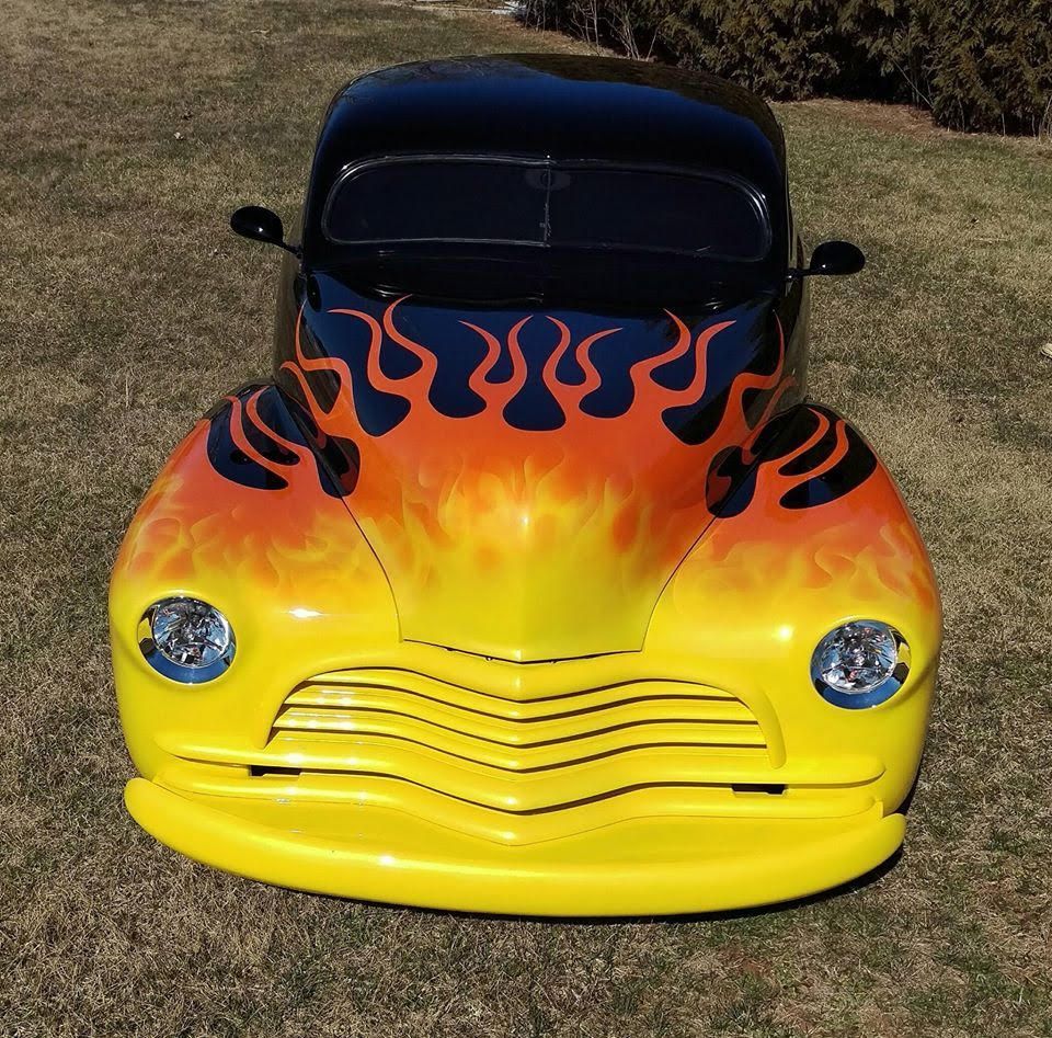 Yellow and flame-painted hot rod car, parked on grass.