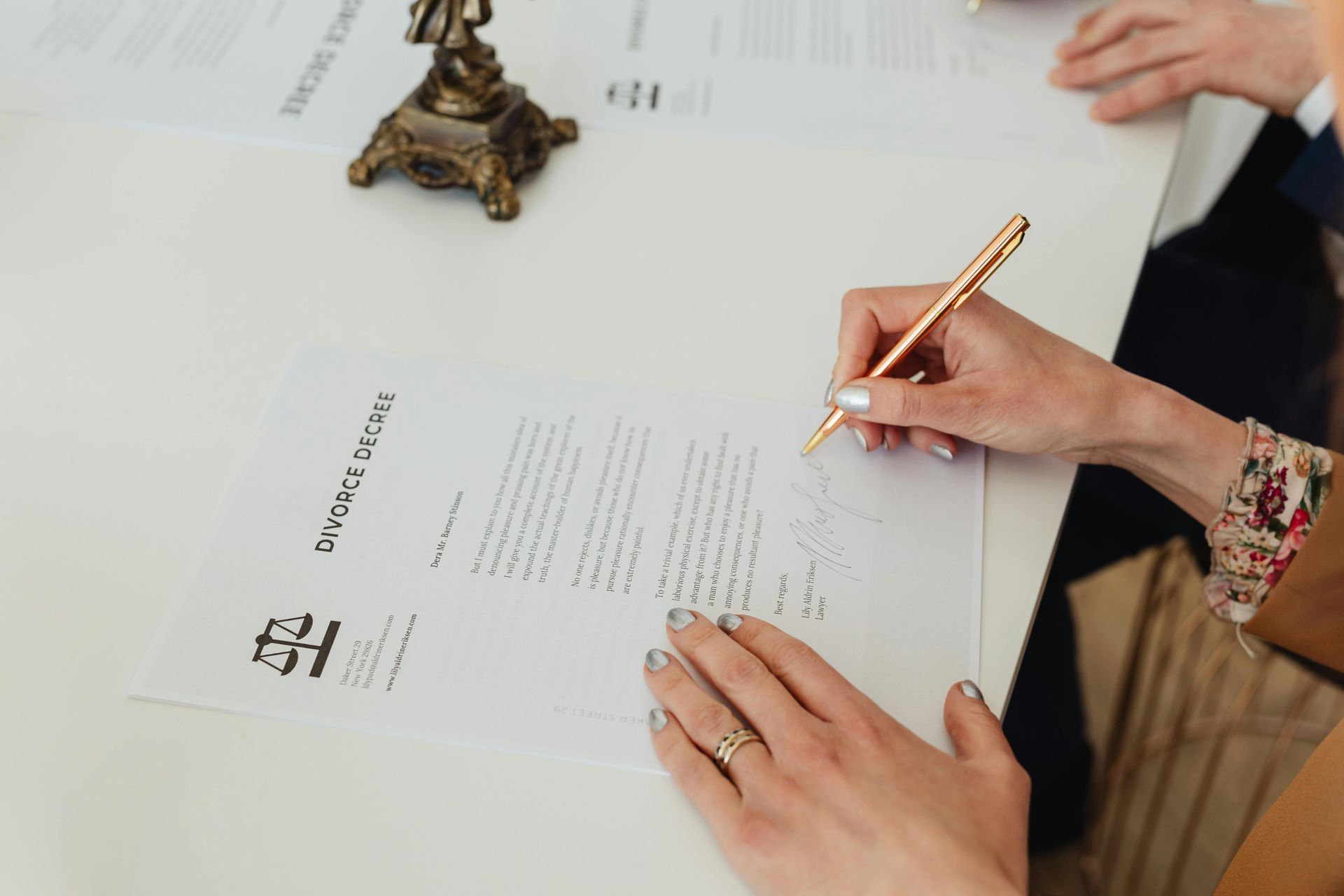 Person signing a legal document at a desk, with a justice statue nearby.