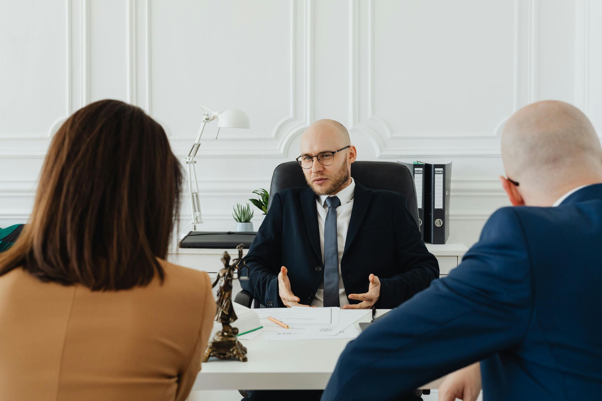 A lawyer in a suit talks to a couple, likely discussing legal matters, in an office setting.