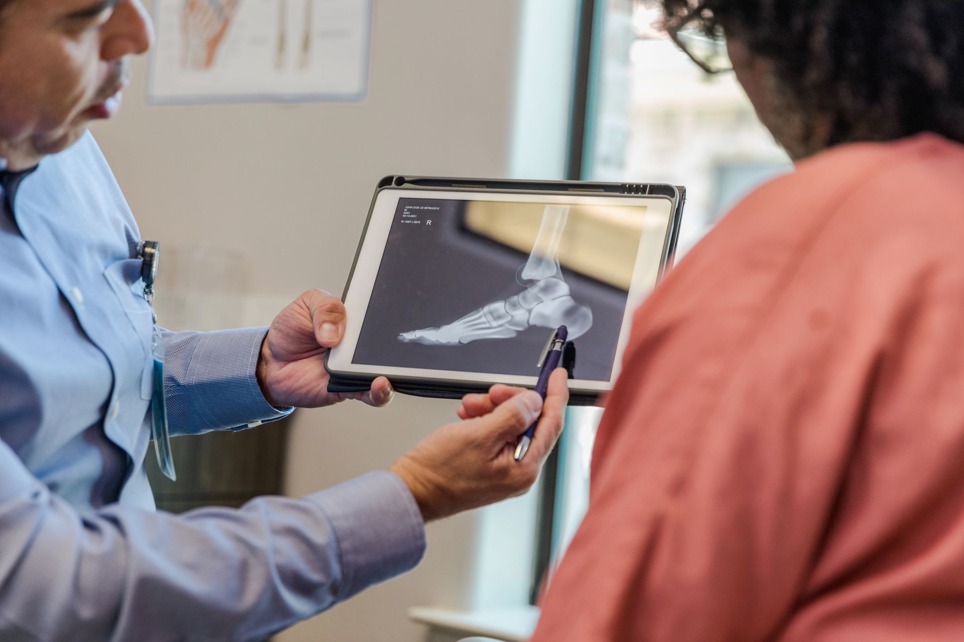 Medical professional showing a foot X-ray on a tablet during a consultation.