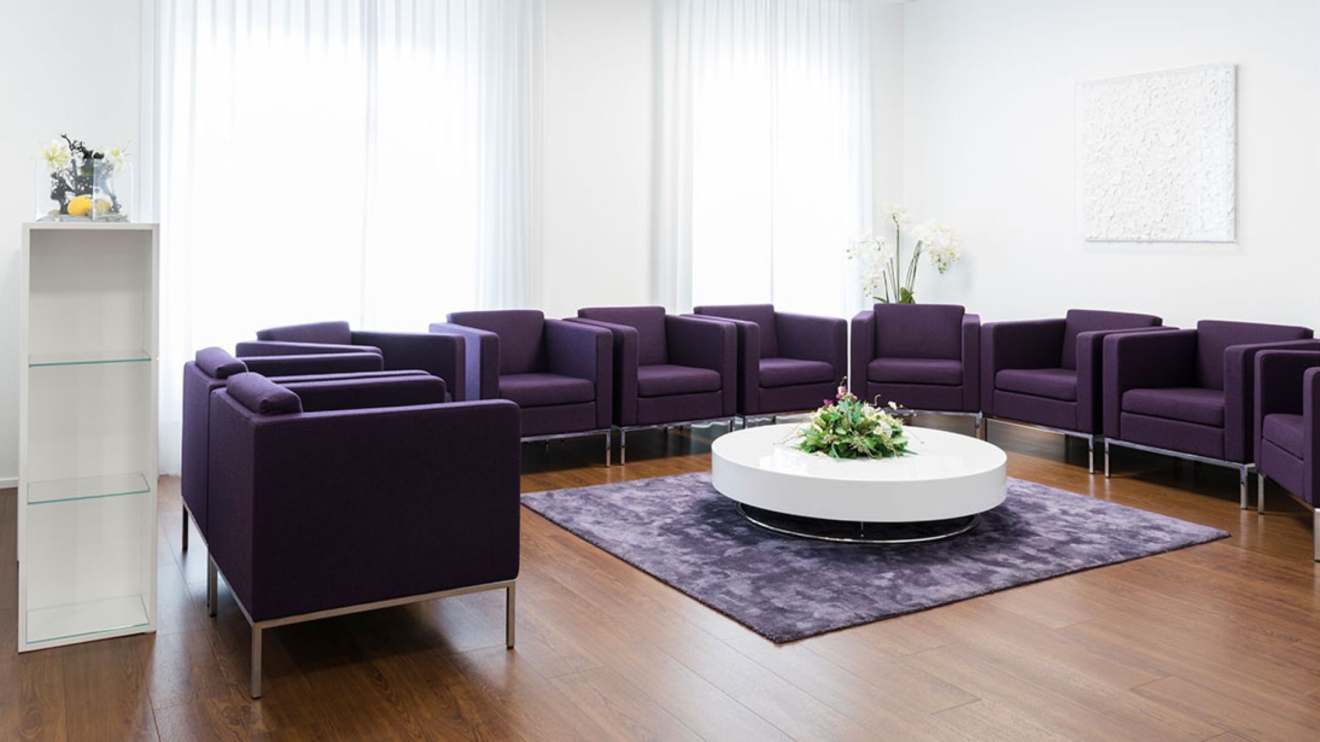 Wartezimmer mit lila Stühlen und einem weissen Tisch