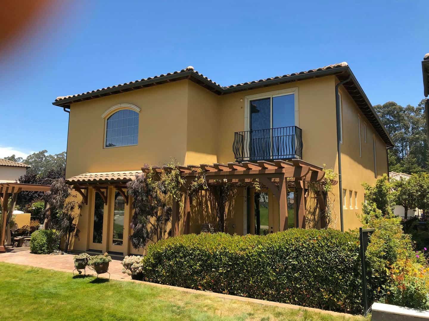 A large yellow house with a lot of windows and a pergola in front of it.