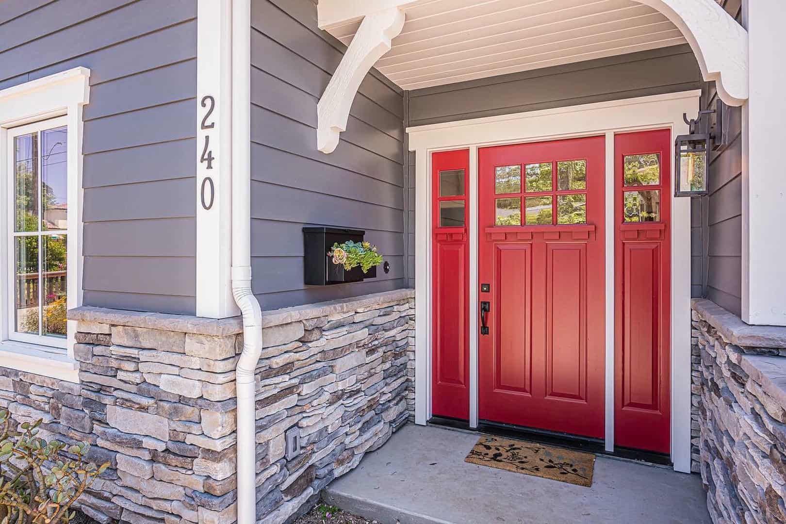The front door of a house with a red door and a stone wall.