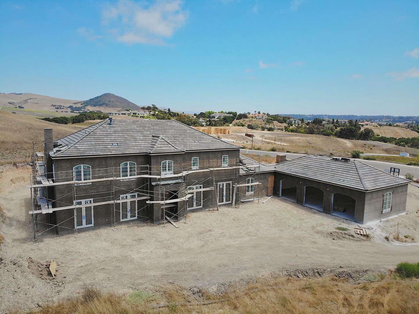 A large house is being built in the middle of a dirt field.