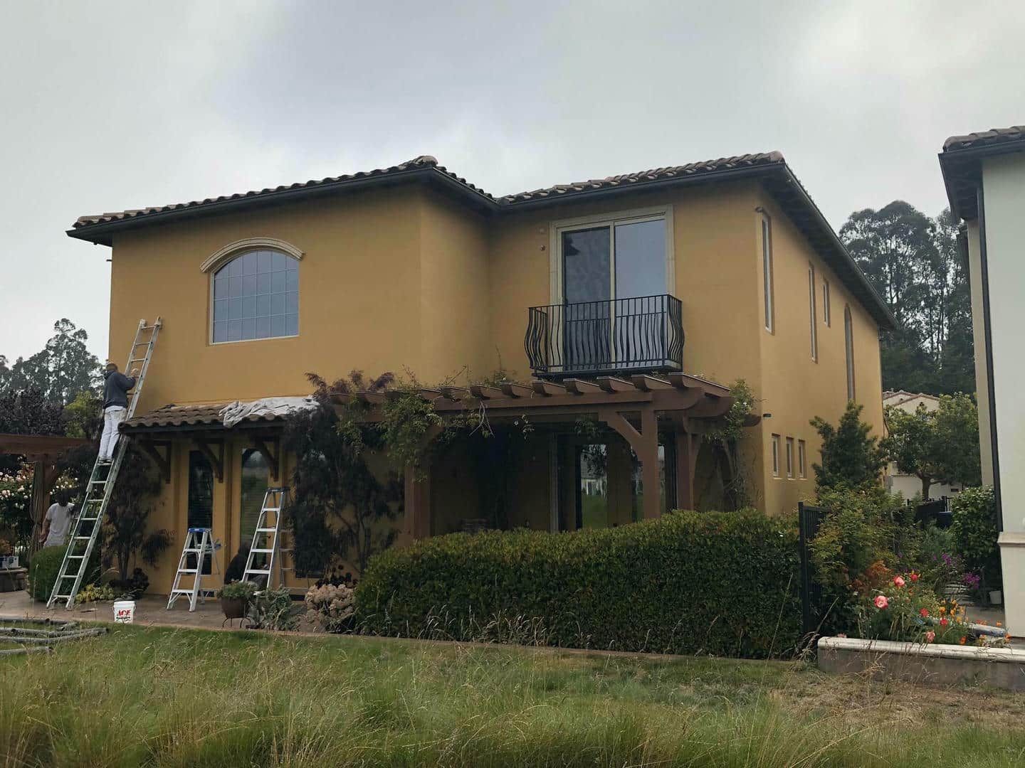 A large yellow house is being painted by a man on a ladder.