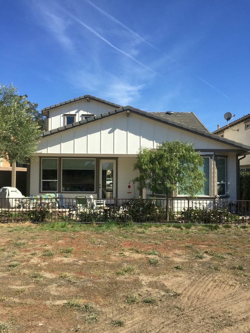 A white house with a lot of windows is sitting on top of a dirt field.
