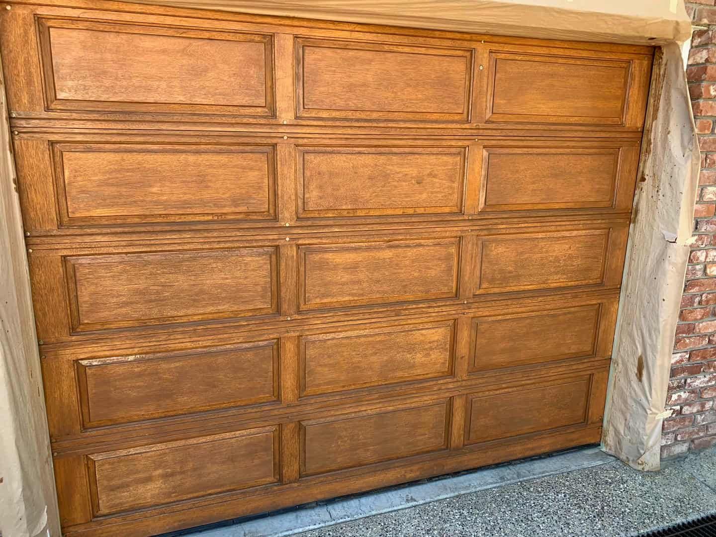 A wooden garage door is sitting next to a brick wall.