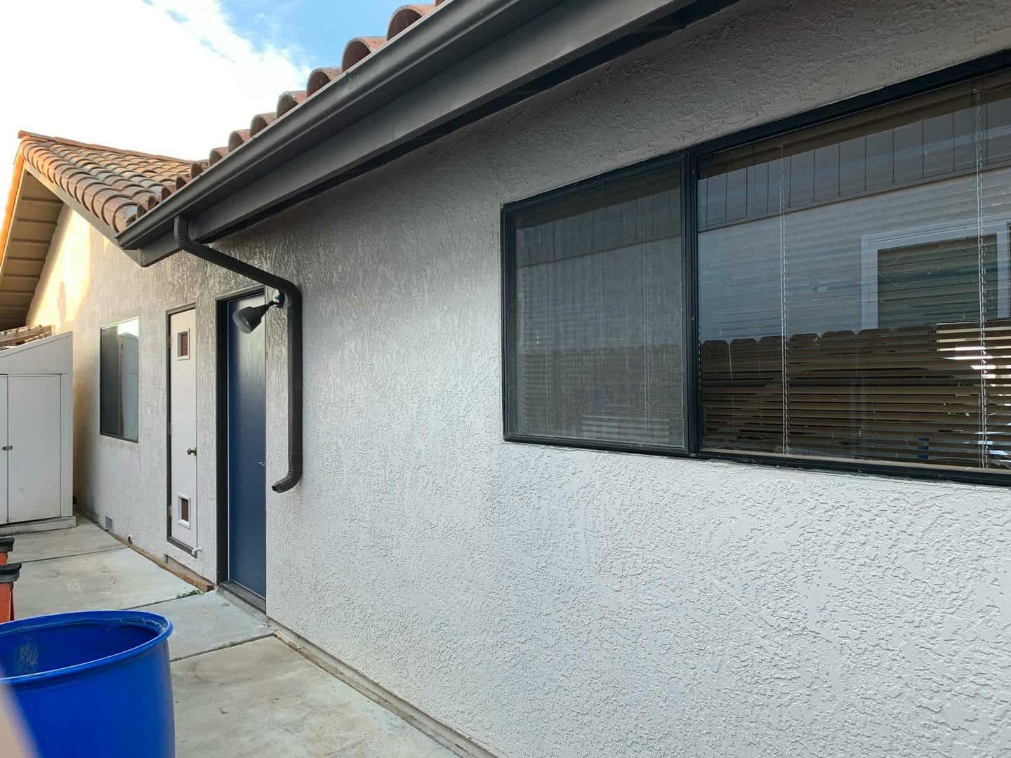 A white house with a blue trash can in front of it.