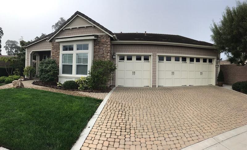 A house with two garage doors and a brick driveway.