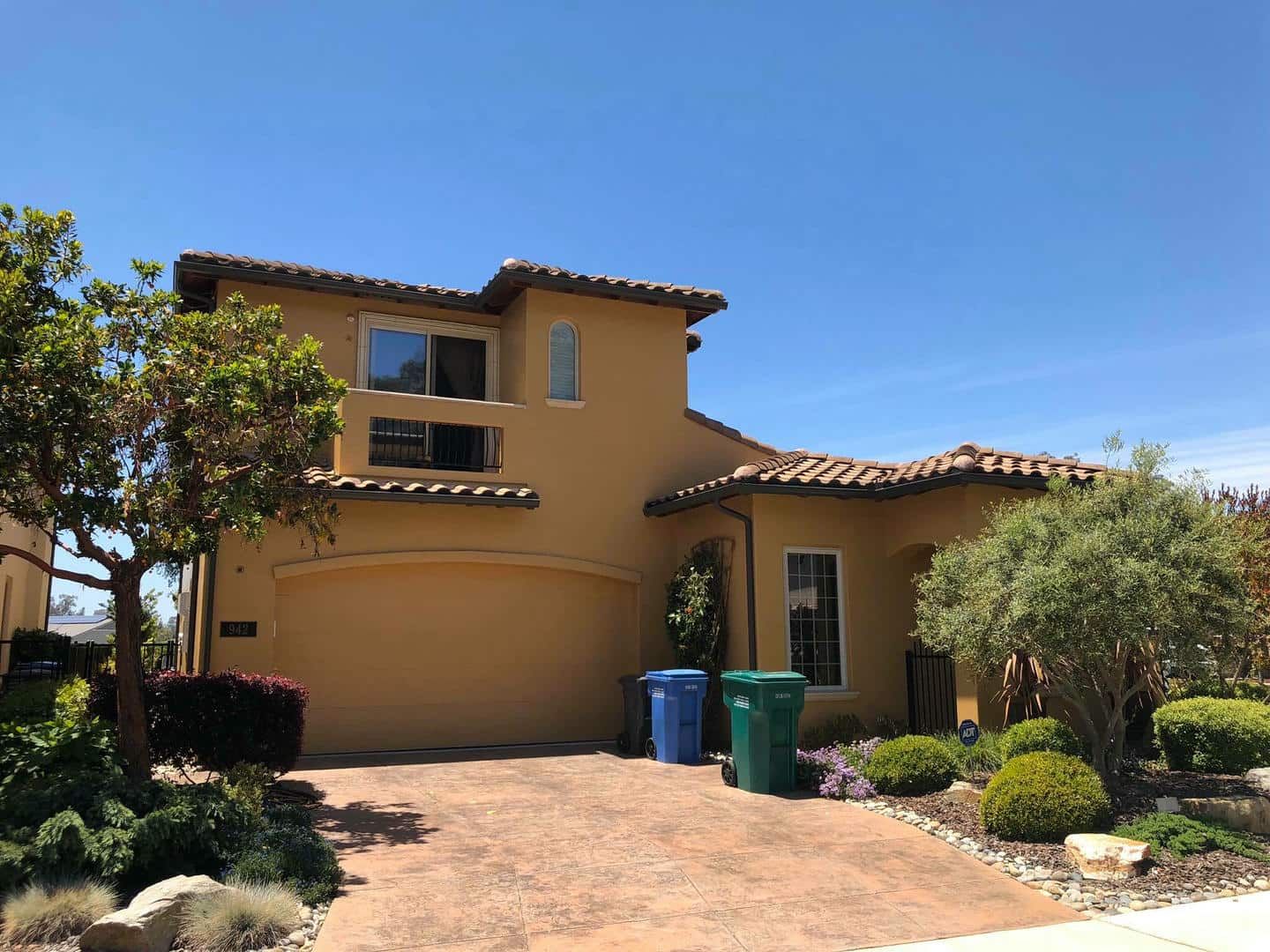A large yellow house with two trash cans in front of it.