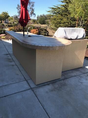A large outdoor kitchen with a red umbrella and a grill.