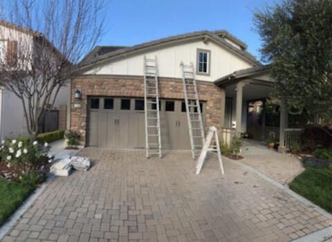 Two ladders are sitting in front of a house that is being painted.