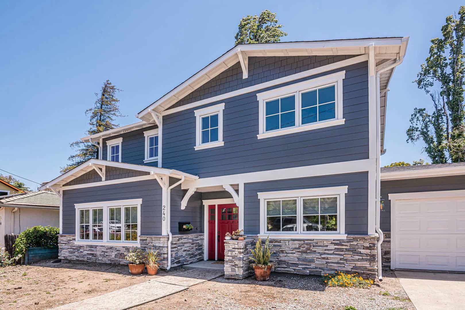 A large gray house with a red door and a white garage.