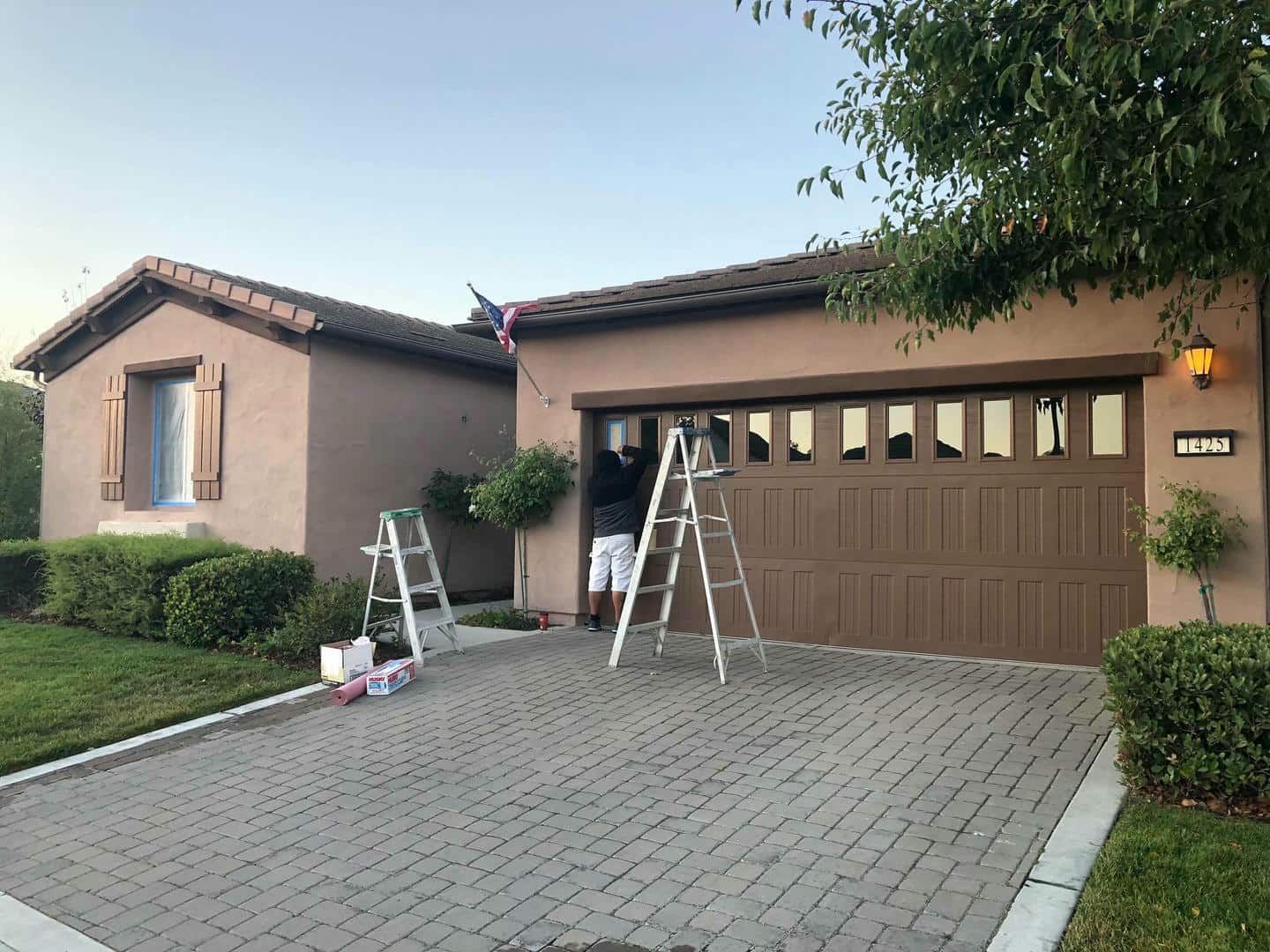 A man is painting the garage door of a house.