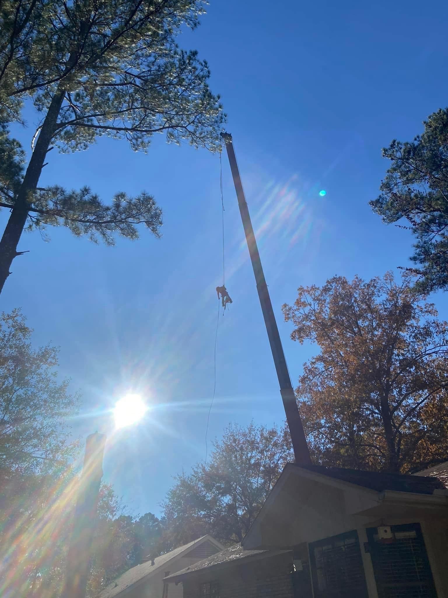 A person on a lift working on a tall pole against a bright blue sky.