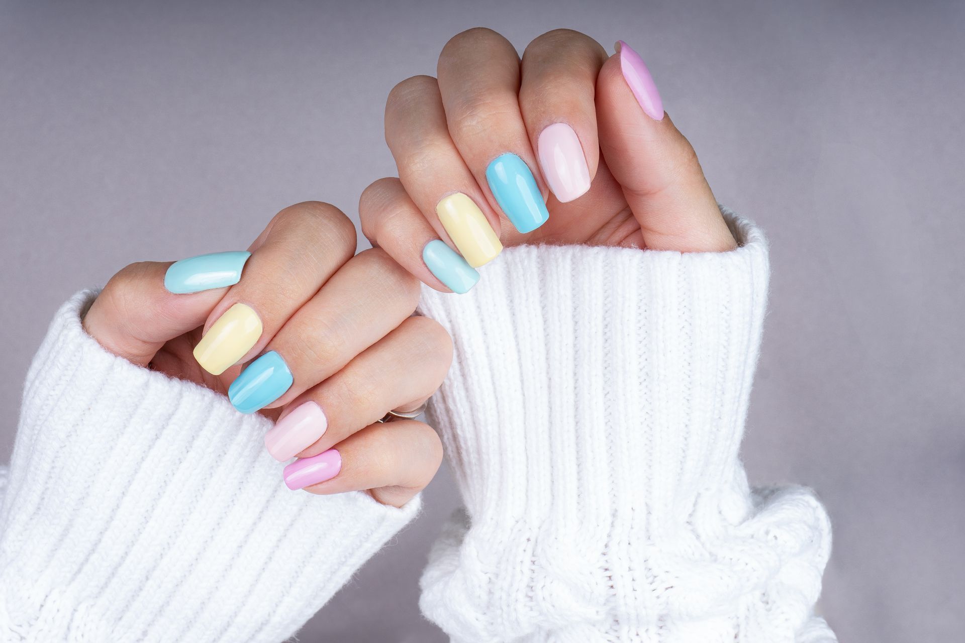 Eine Frau trägt einen weißen Pullover und hat bunte Nägel.