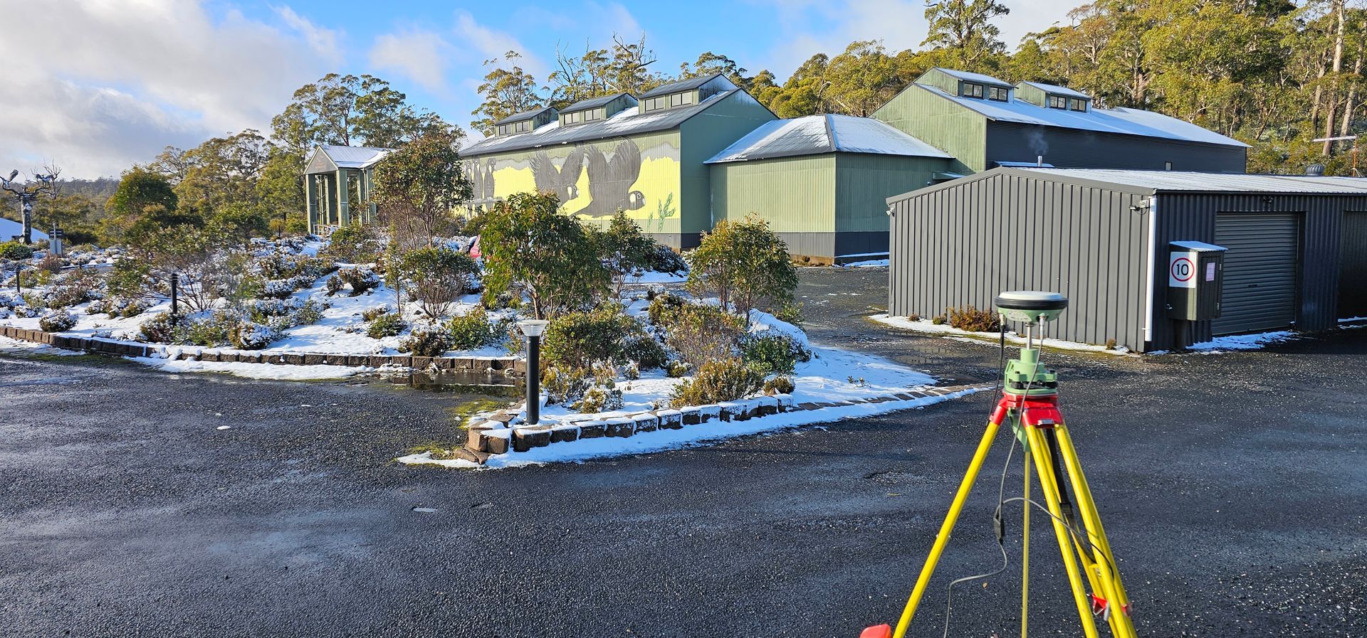A theodolite is sitting on a tripod on the side of a road.