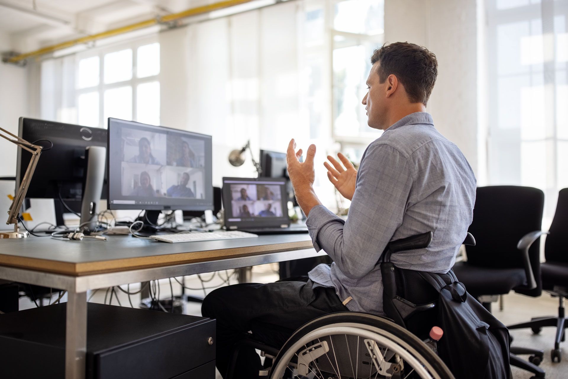 A man in a wheelchair is sitting at a desk in front of a computer.