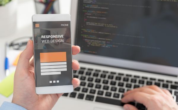 A person is holding a cell phone in front of a laptop computer.