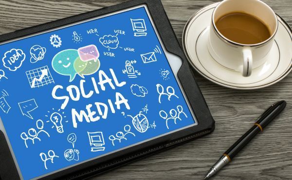 A tablet with social media written on it next to a cup of coffee and a pen.
