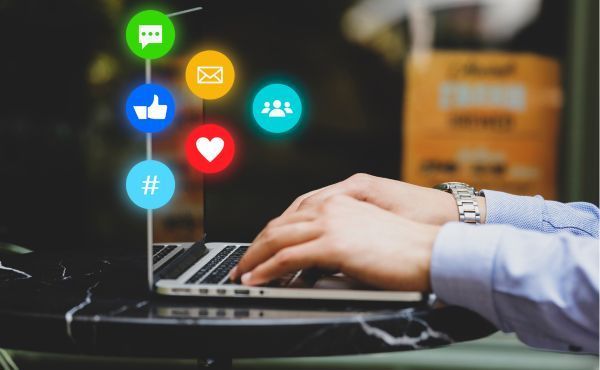 A person is typing on a laptop with social media icons coming out of the screen.