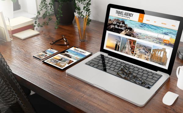 A laptop computer is open to a travel agency website on a wooden desk.
