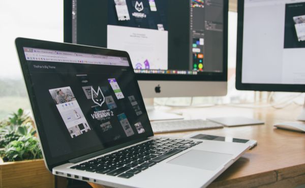 A laptop computer is sitting on a desk next to two monitors.