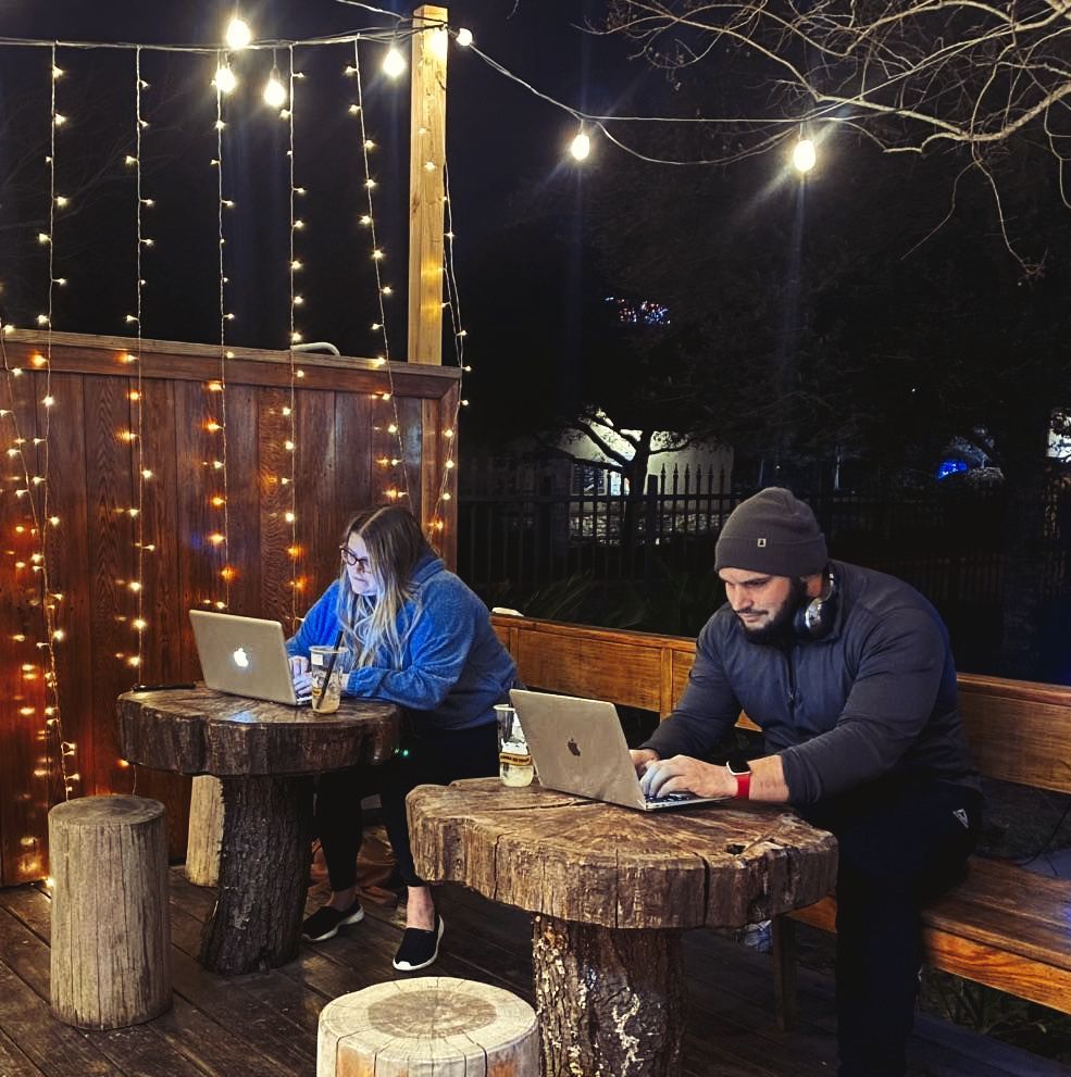 A man and a woman sit at wooden tables with laptops