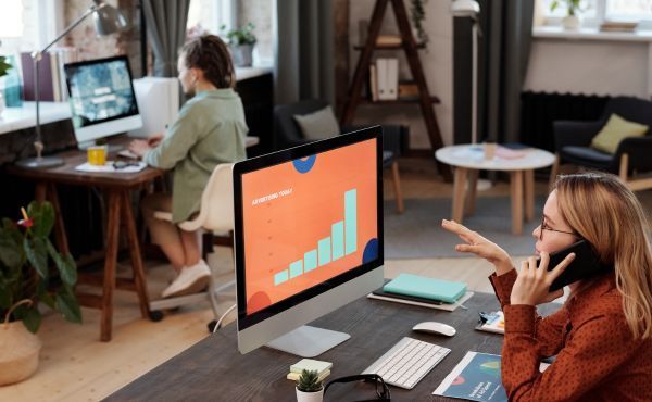 A woman is sitting at a desk in front of a computer talking on a cell phone.