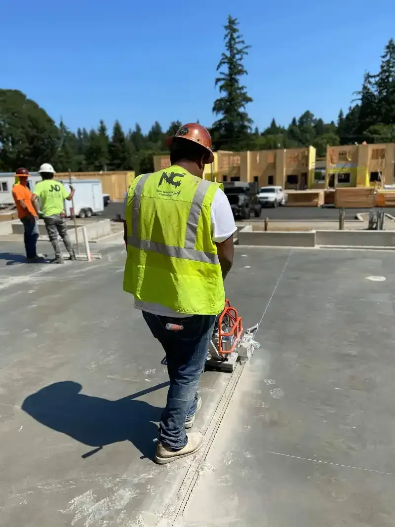 A construction worker wearing a yellow vest and hard hat is cutting concrete in Vancouver, WA by NAVA Concrete LLC