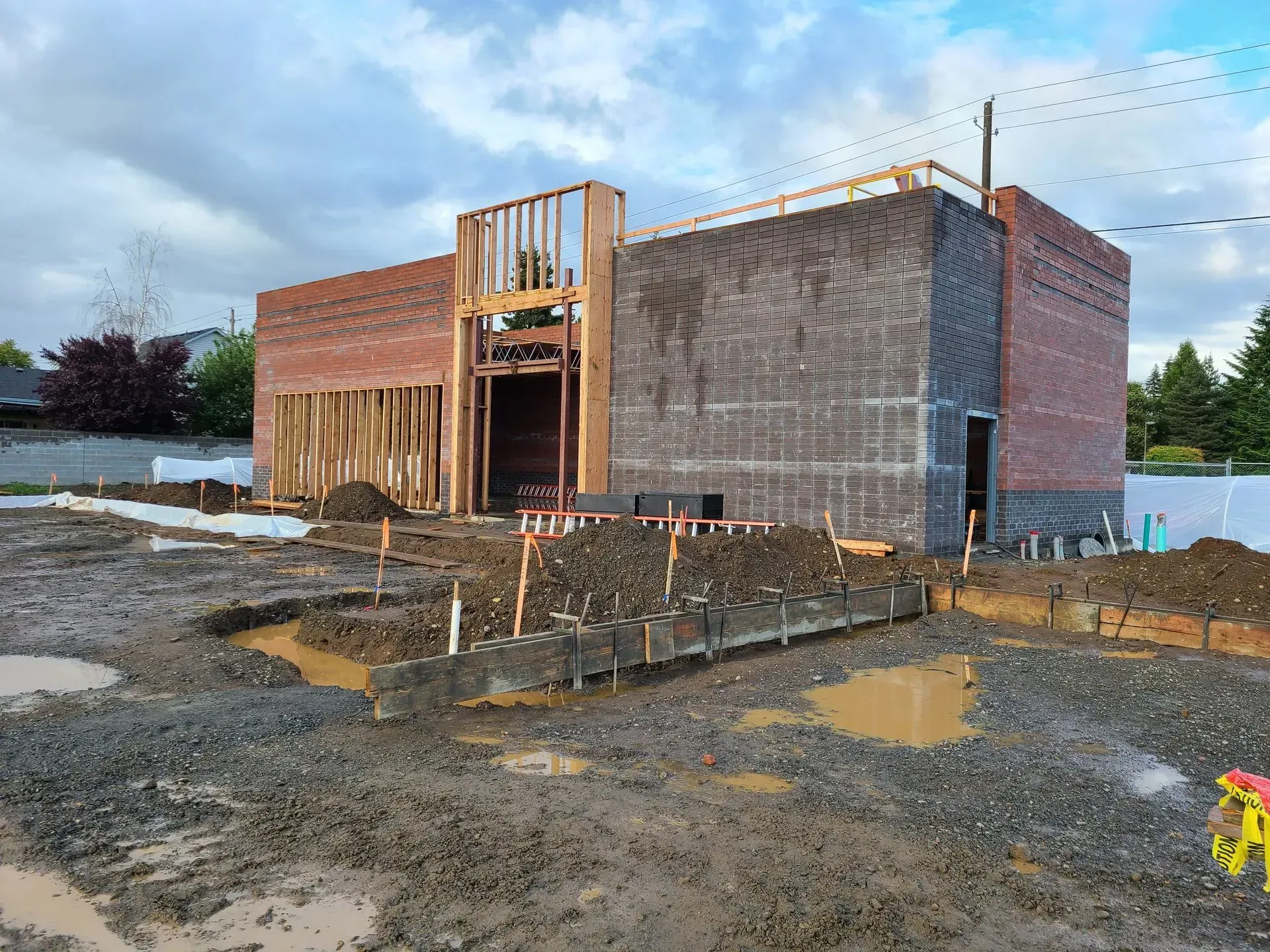A large brick building is being built in a muddy area.