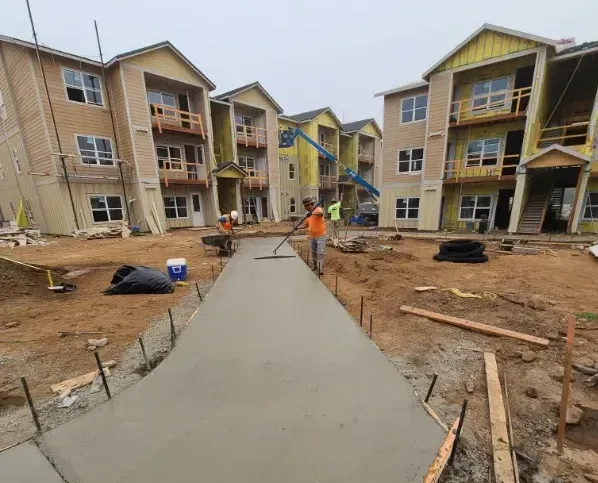 Construction workers smoothing wet concrete sidewalk at an apartment complex under construction.