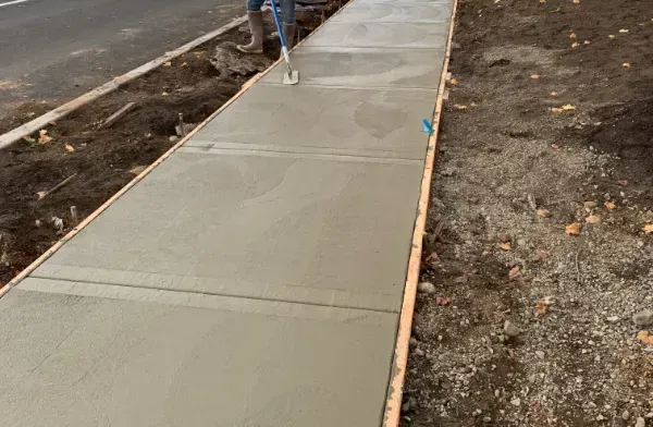 Person smoothing wet concrete sidewalk with a trowel.
