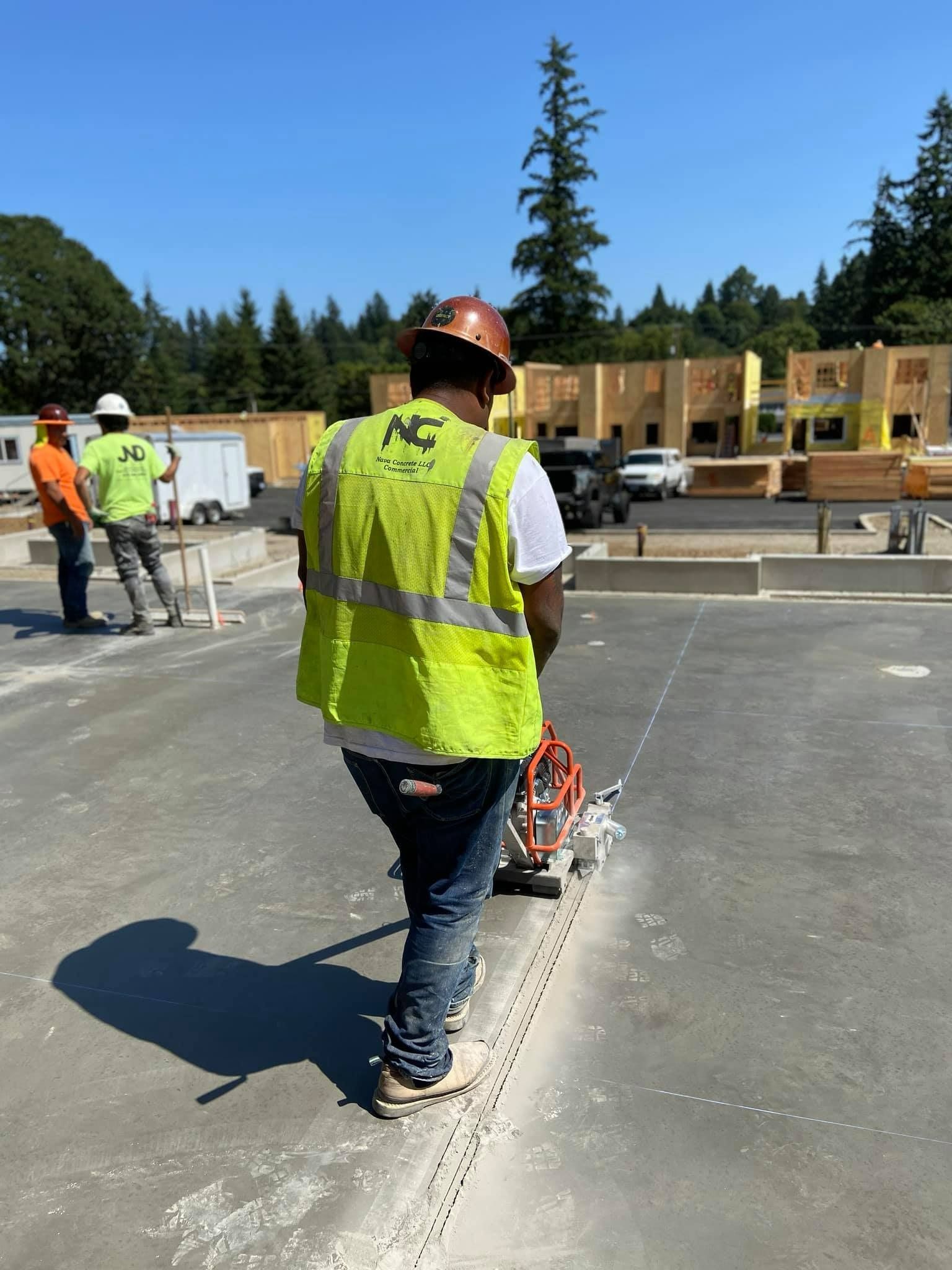 A construction worker wearing a yellow vest and hard hat is cutting concrete.