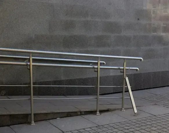 Stainless steel handrails next to a ADA ramp against a grey brick wall.
