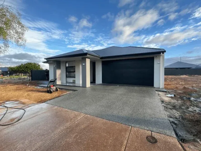 Modern house with black garage door, concrete driveway, and blue sky in Portland OR.