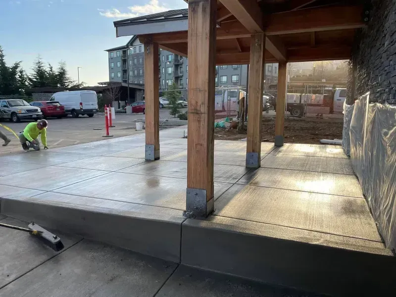 A man is working on a concrete walkway under a wooden structure.