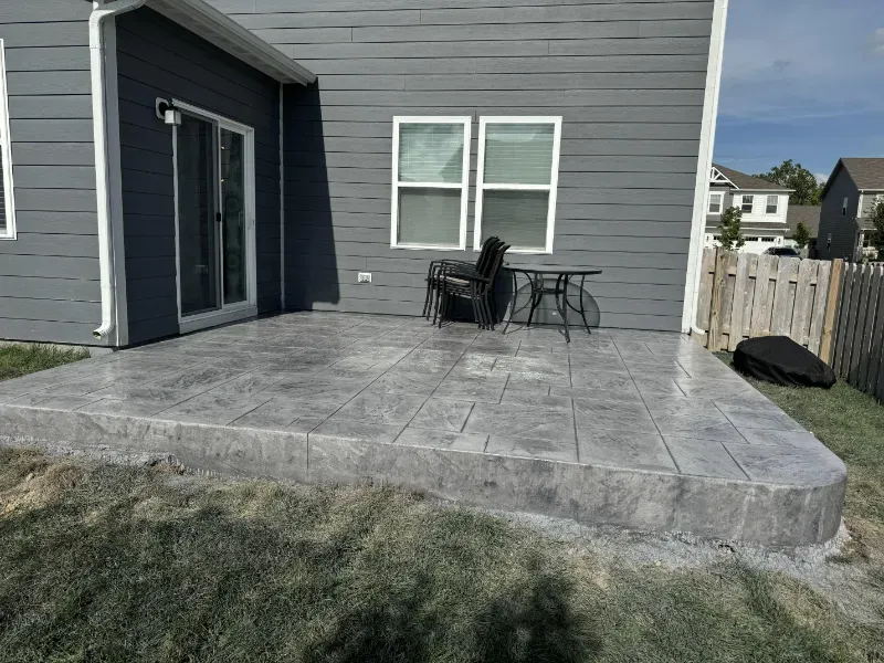 A concrete patio with a table and chairs in front of a house.