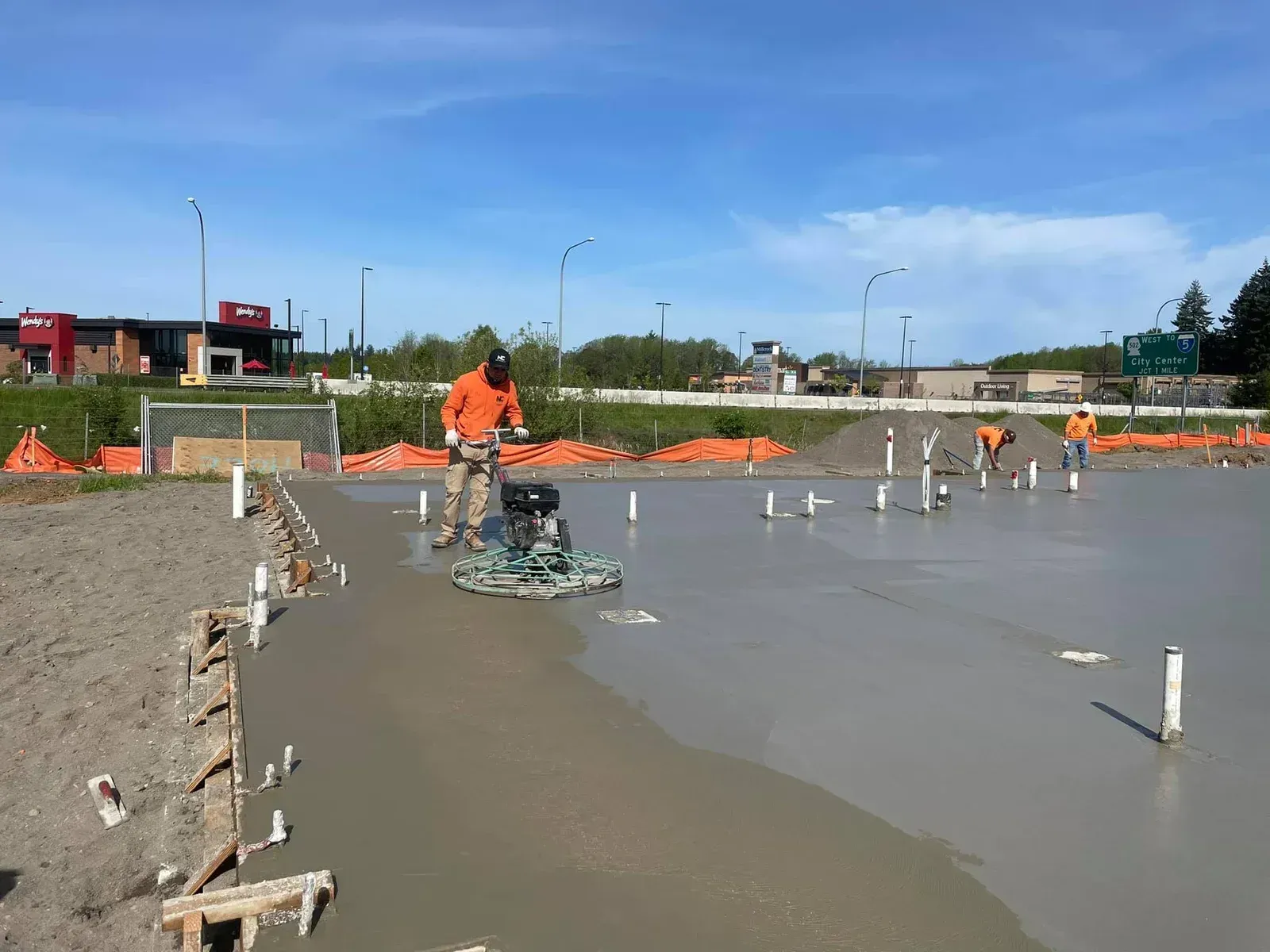 Construction workers finishing a freshly poured concrete slab using a power trowel during a commerci