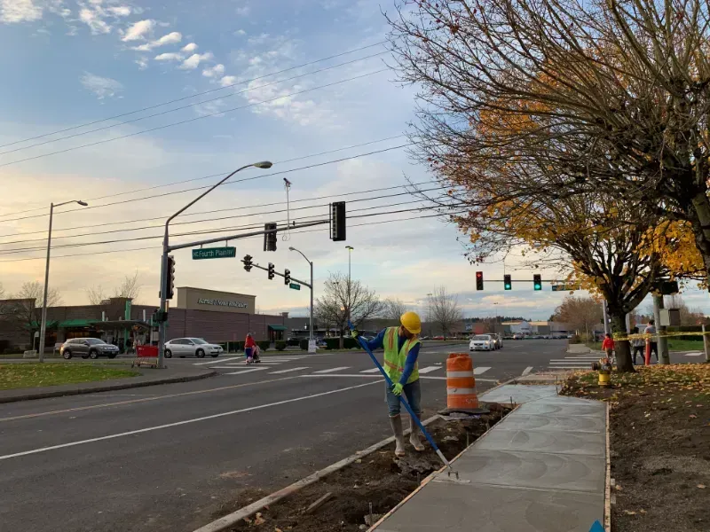 Construction worker raking soil near a  concrete sidewalk by a road in Vancouver WA.