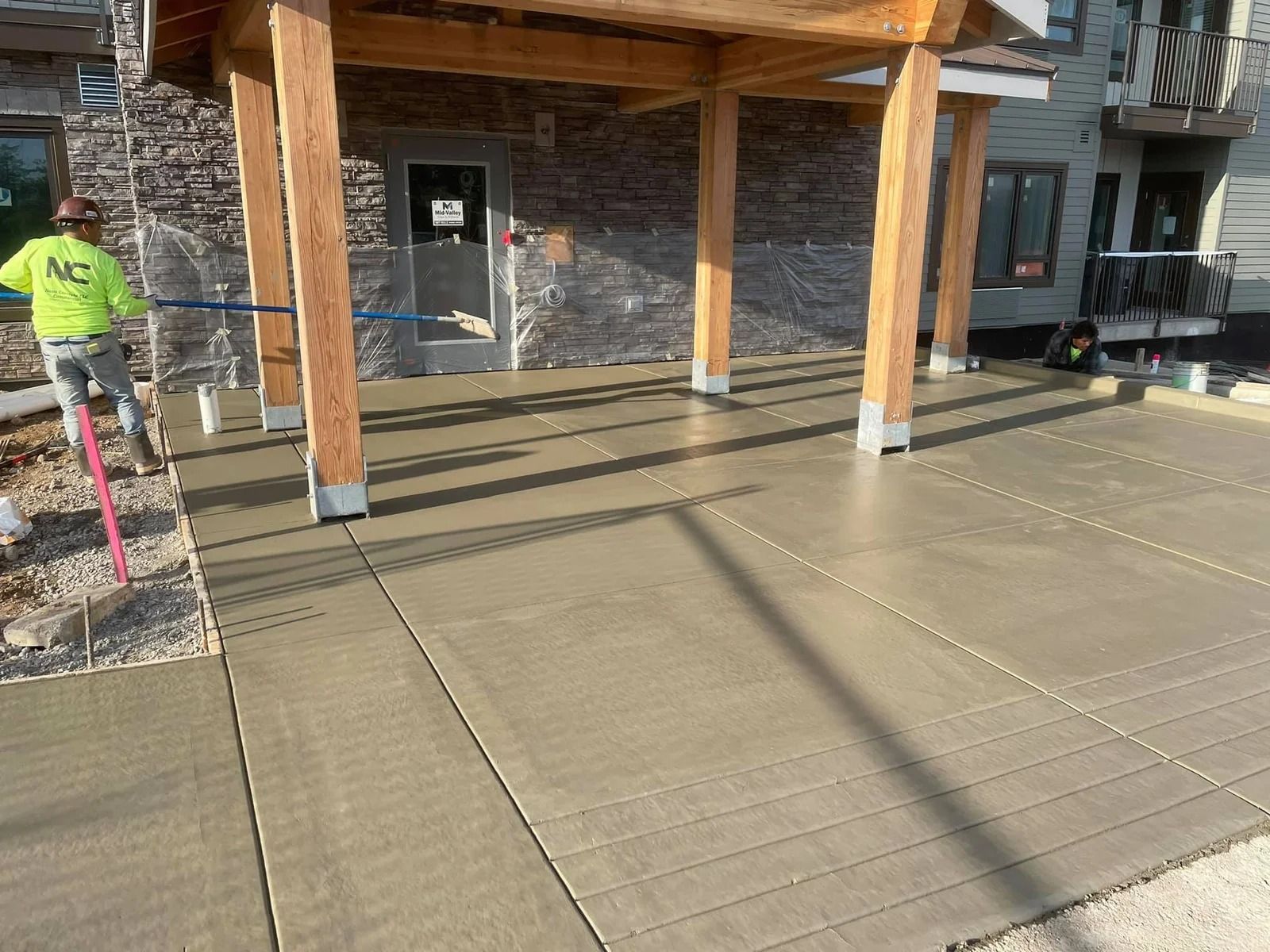 A man is working on a concrete driveway in front of a building in Vancouver, WA by NAVA Concrete LLC