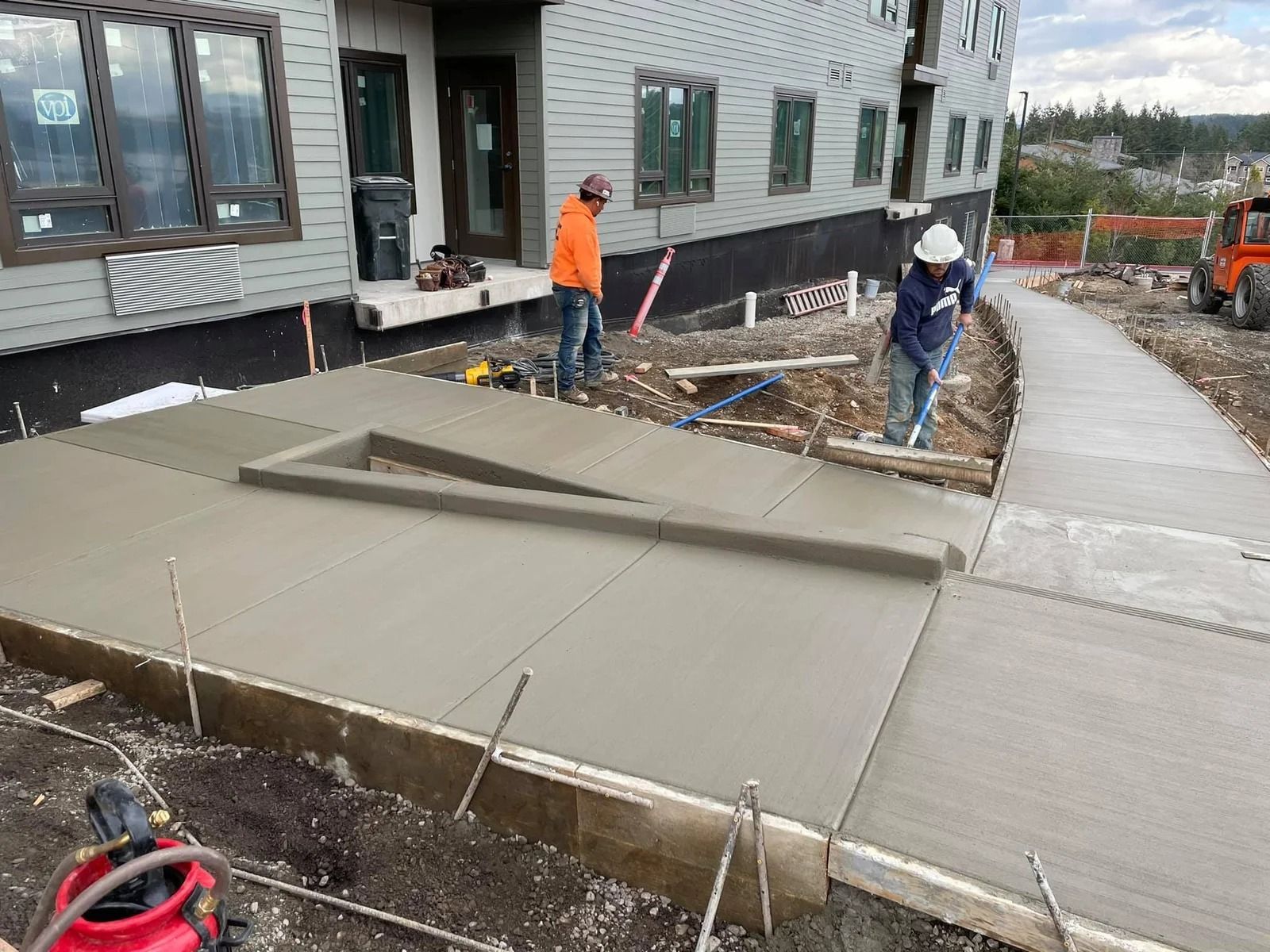 A group of construction workers are working on a sidewalk in front of a building in Vancouver, WA by NAVA Concrete LLC