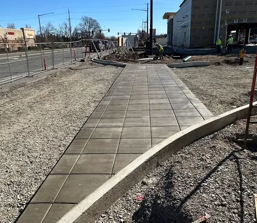 Pathway construction with stamped concrete. Gravel, curb, and building in the background in Portland OR.